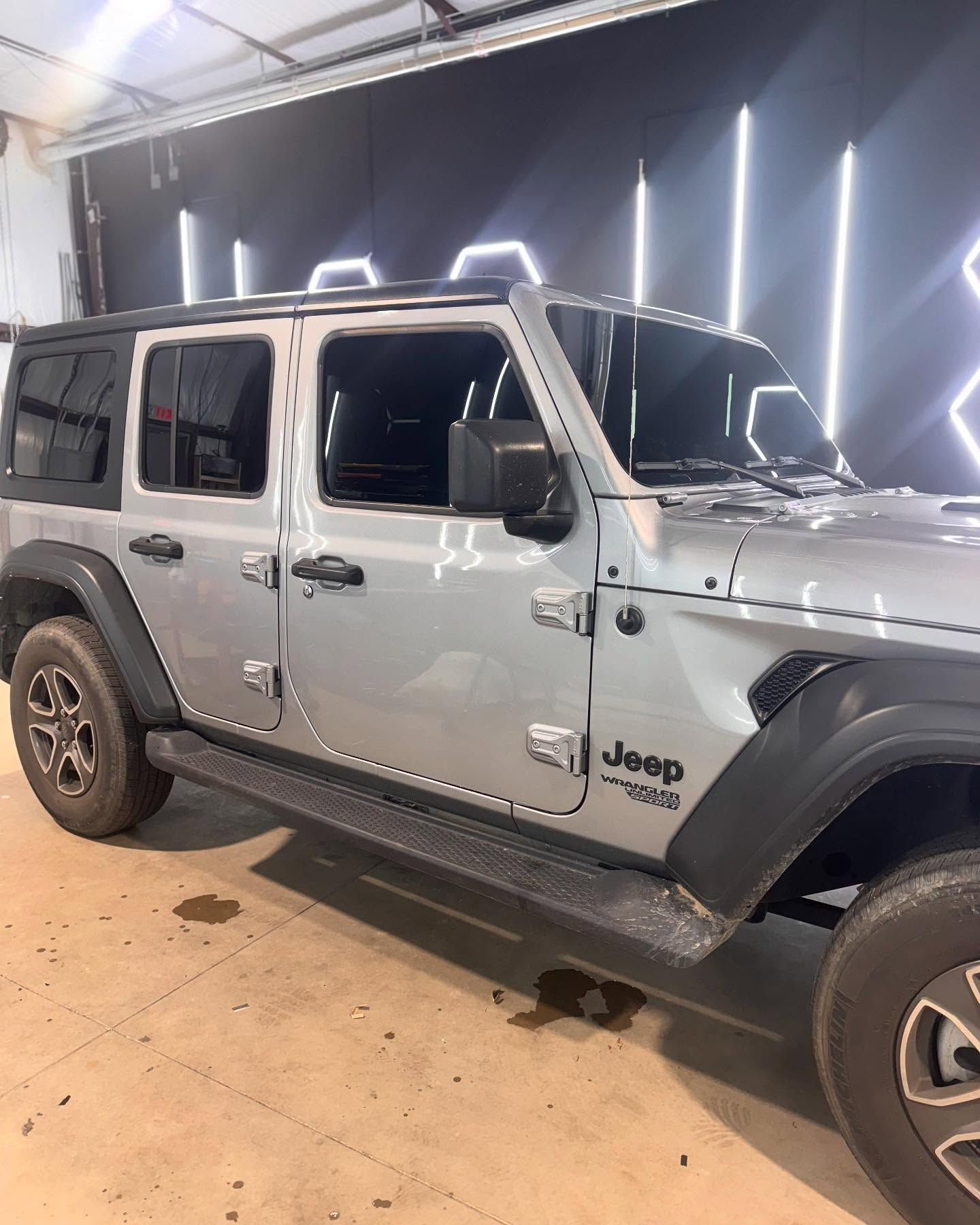 Silver Jeep Wrangler parked indoors, side view.