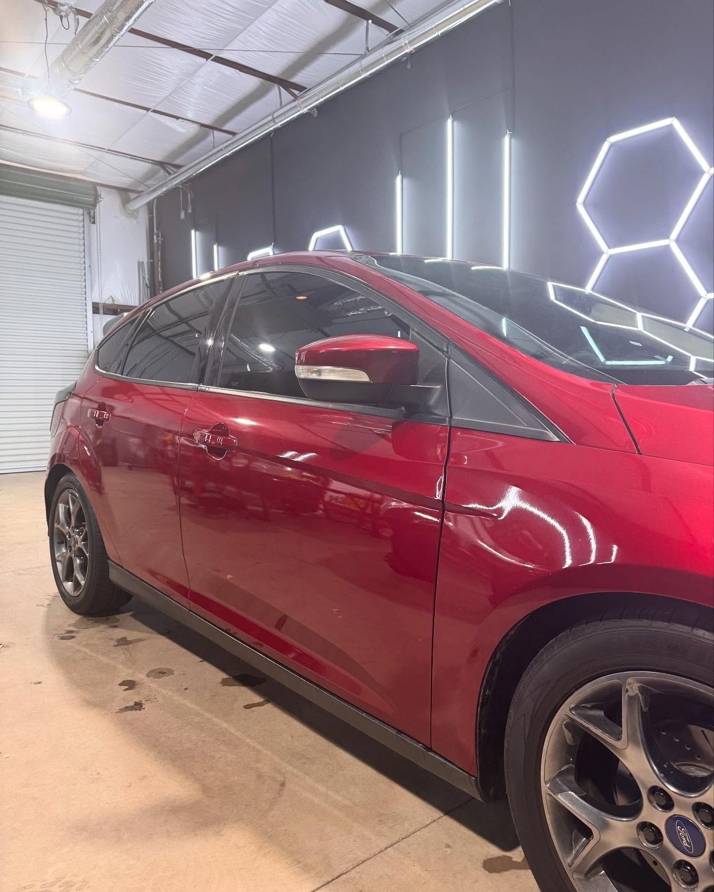 Red Ford Focus hatchback inside a garage, next to decorative wall lighting.
