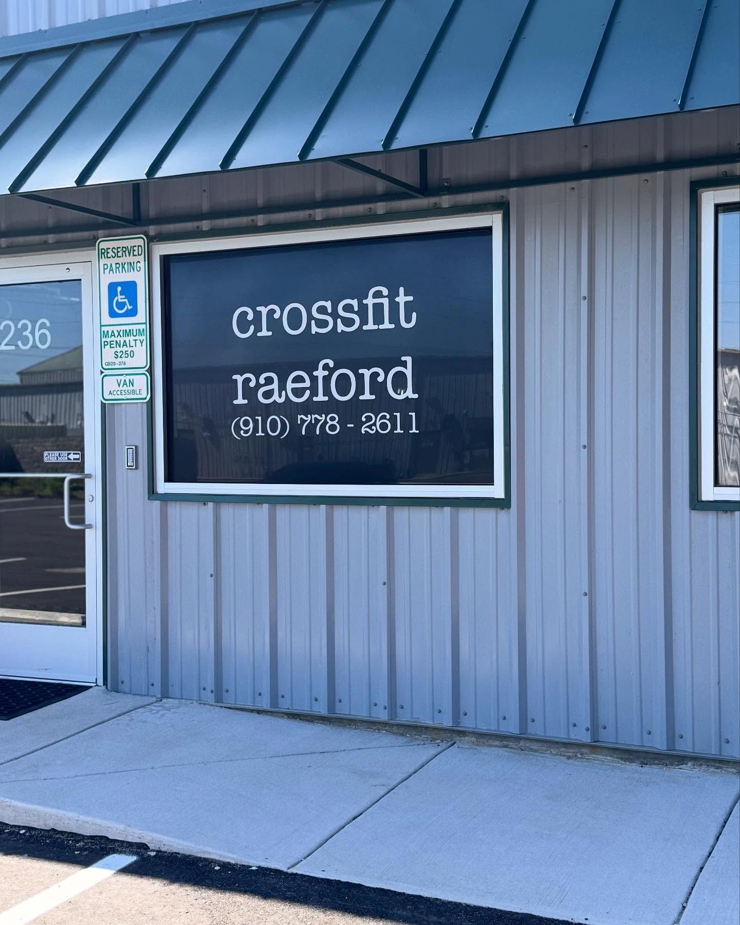 Exterior of CrossFit Raeford gym, with signage in a window. Gray building with green awning.