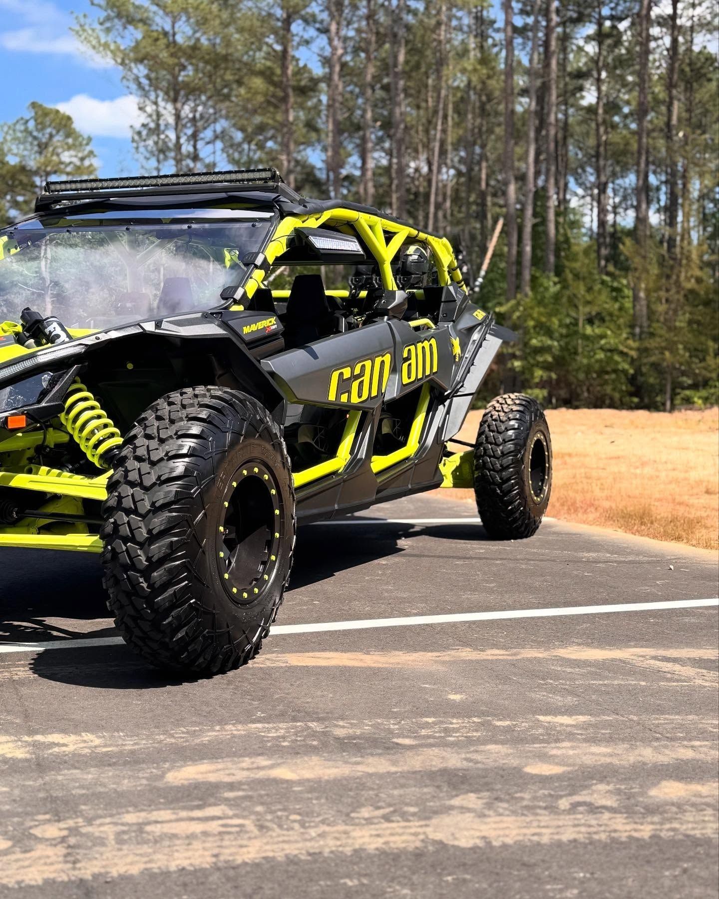 Can-Am side-by-side vehicle with black and neon green accents on a paved area, trees in the background.