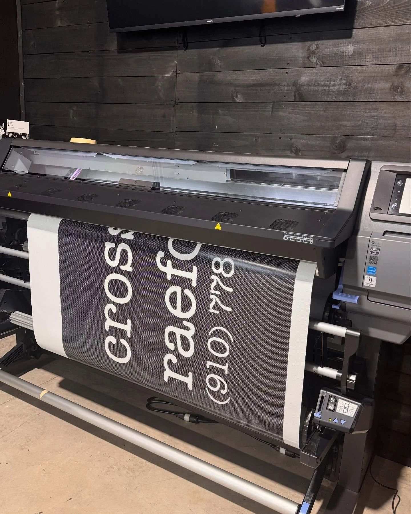 Large format printer printing a black and white banner. Text reads 