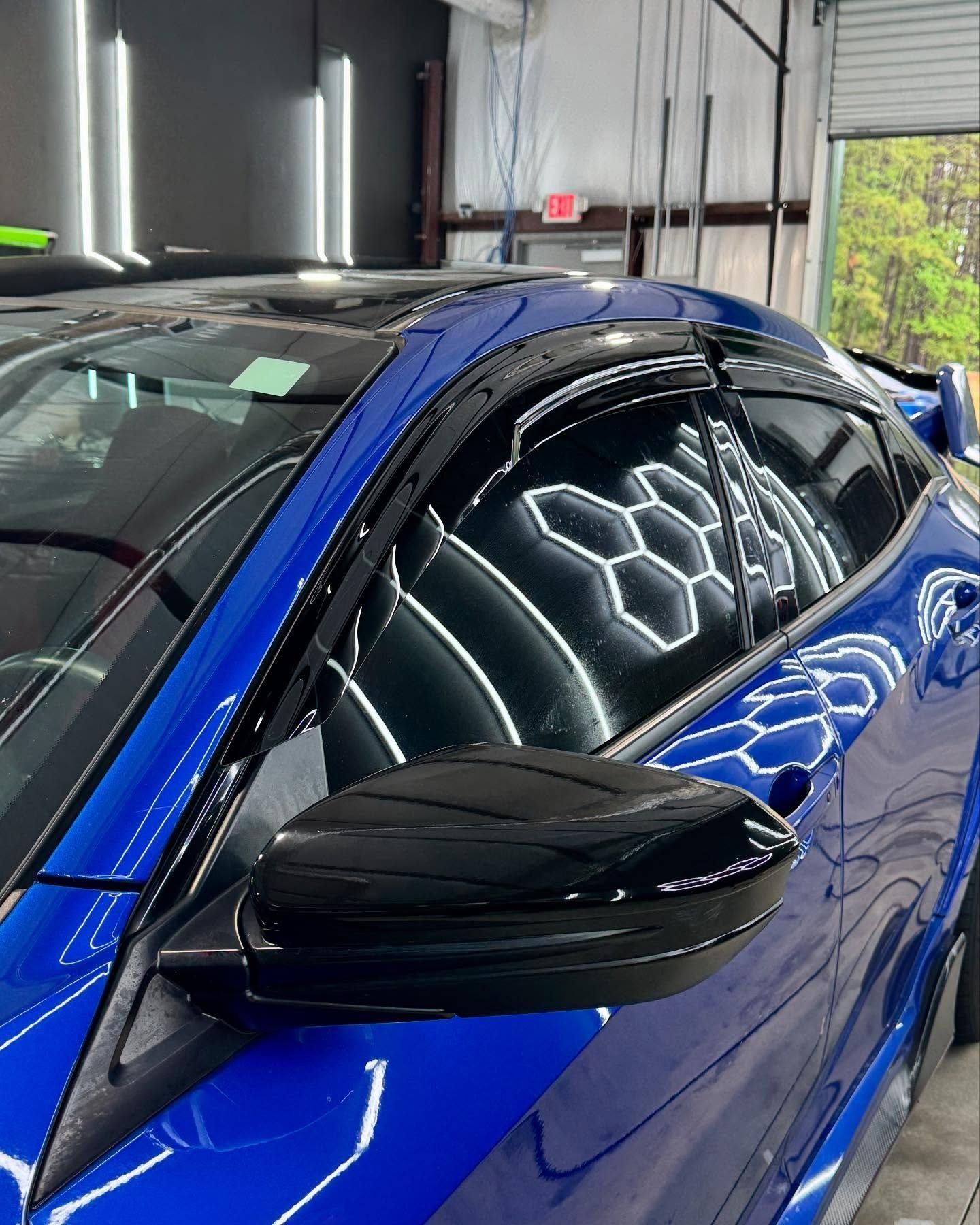 Blue car's side view with black mirror and tinted windows reflecting hexagonal lights.