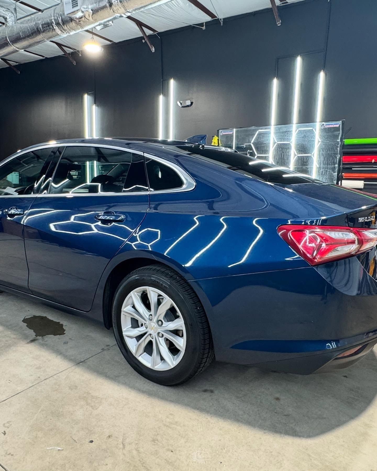Blue sedan parked in a garage with bright lights.