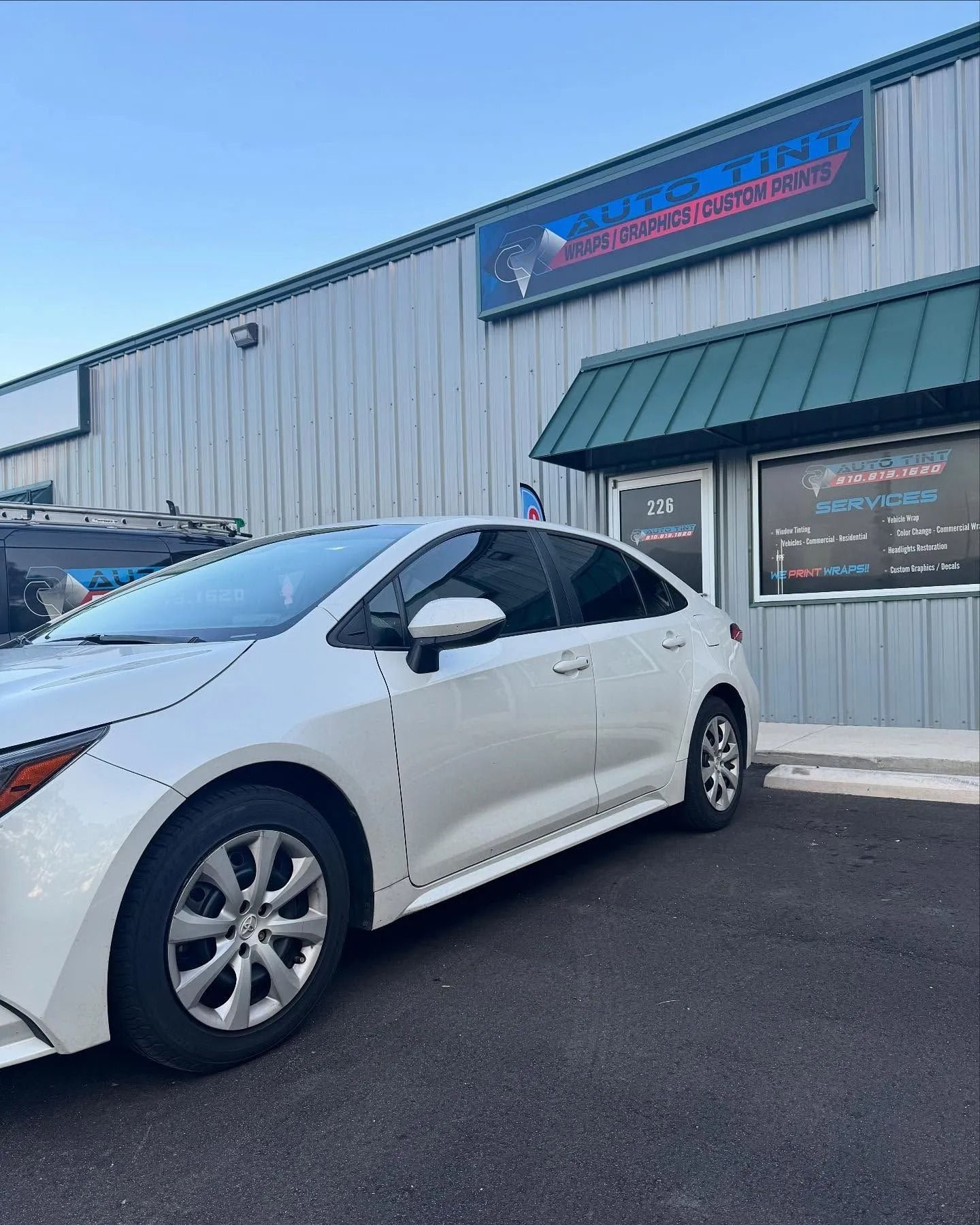 White car parked in front of a building with a business sign.
