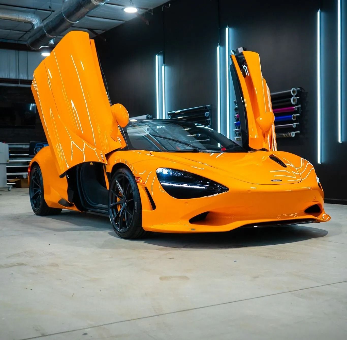 Orange McLaren sports car with doors open, in a garage.