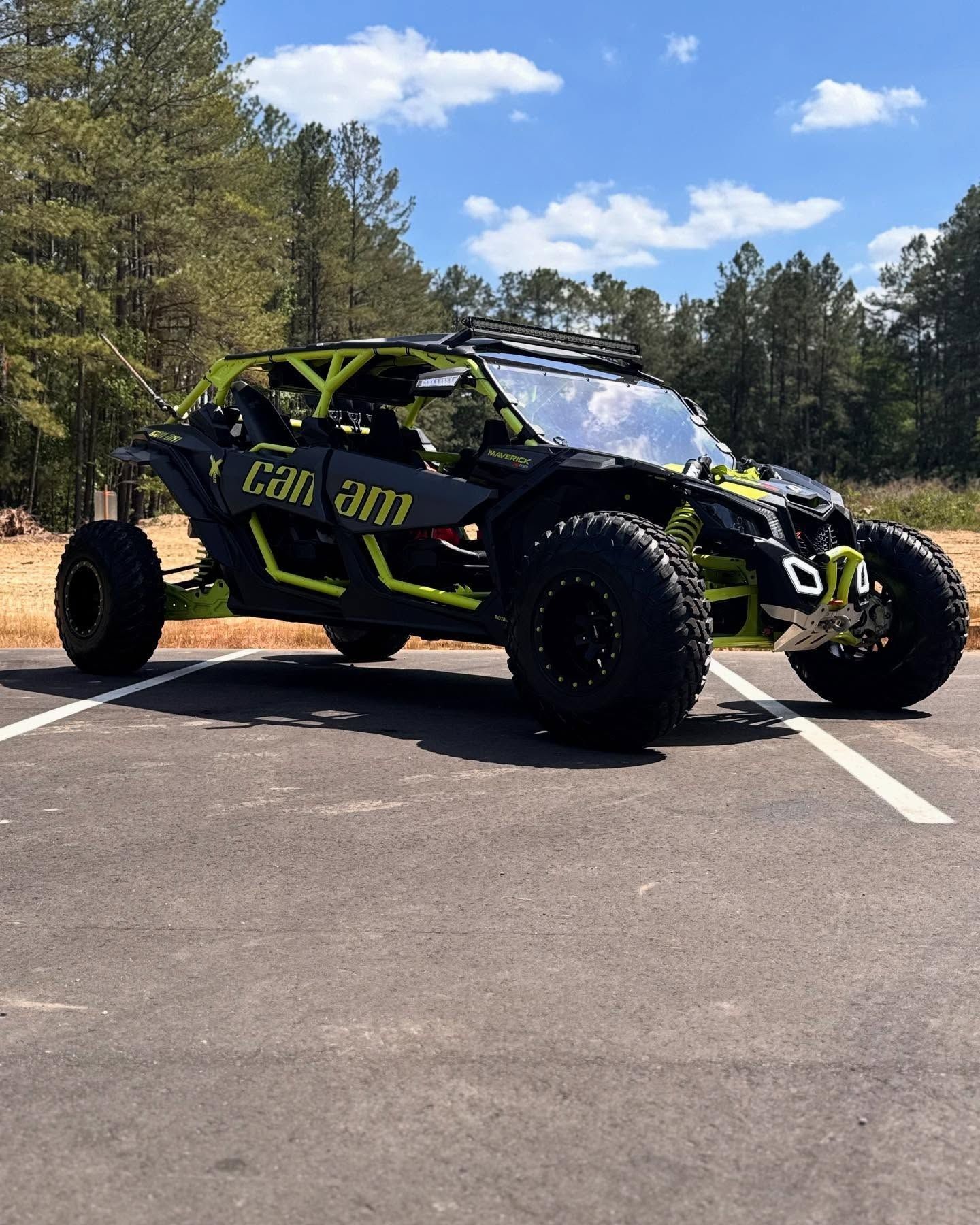Black and neon green Can-Am Maverick X3 side-by-side on asphalt parking lot, blue sky, trees.