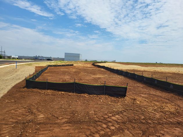 Dirt embankment construction site with black silt fences under a partly cloudy sky