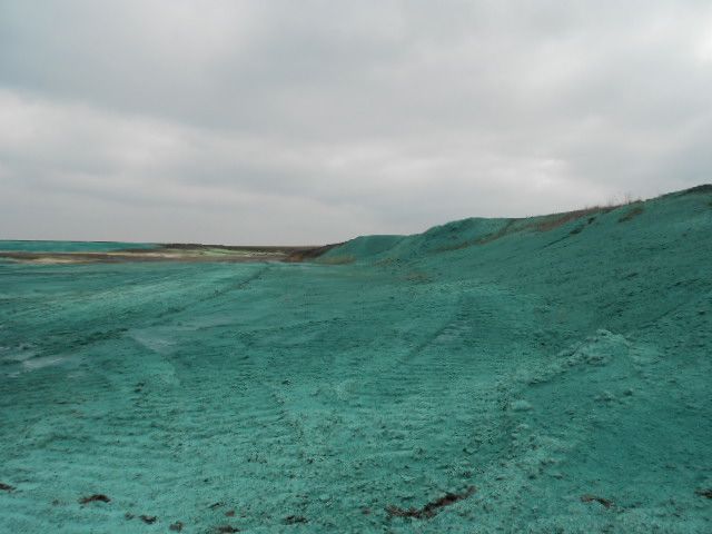 Turquoise rocky shoreline under a cloudy sky, with a low hill in the distance