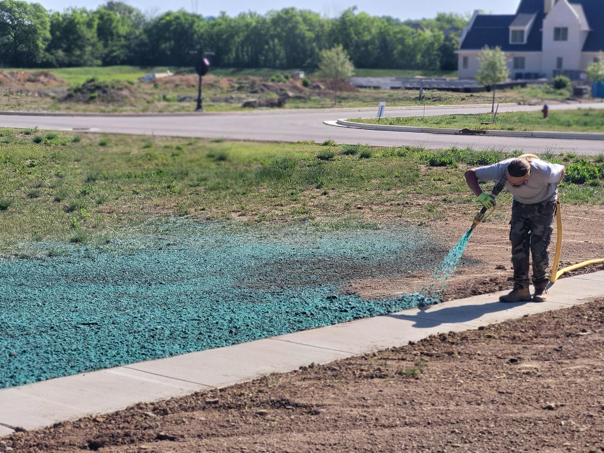 Worker spraying blue coating on a paved area beside a pond in a residential development