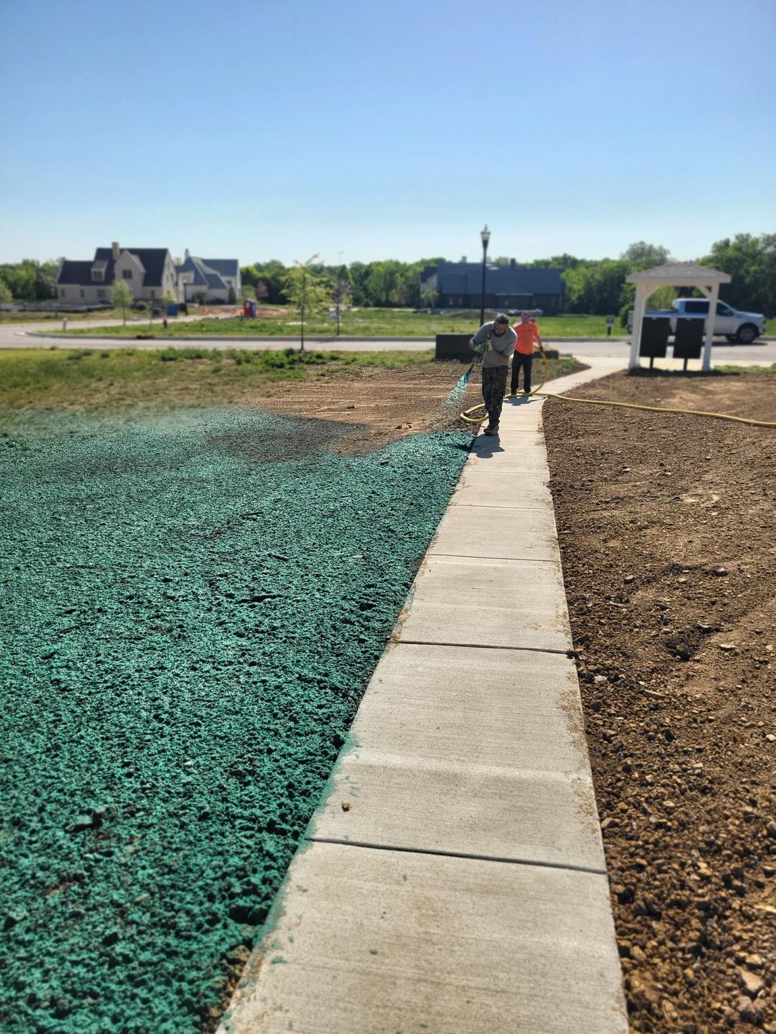 Person walking on a concrete path beside a green ground cover in a sunny construction area