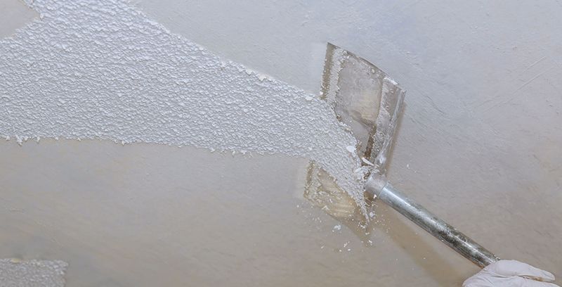A person is using a spatula to spread white paint on a wall.