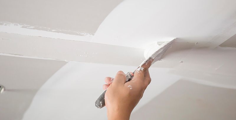 A person is plastering a ceiling with a spatula.