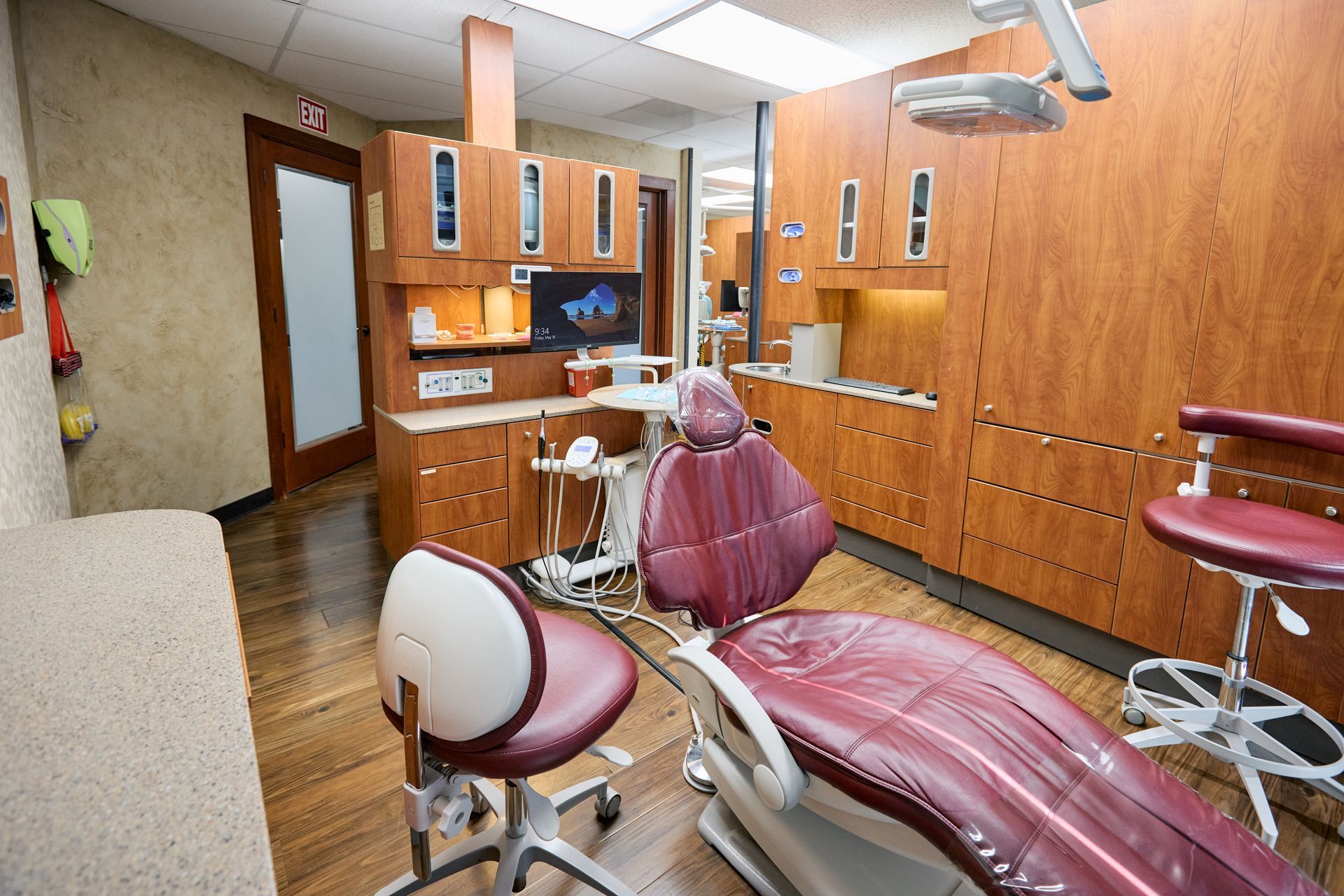 Dental office exam room with maroon chair and cabinets.