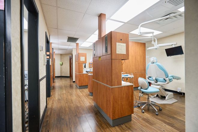 Dental office hallway with dental chair, cabinets, and equipment. Wooden floors and neutral colors.