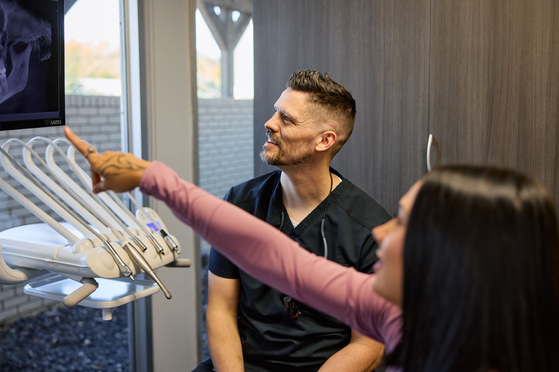 Dentist points at X-ray with patient in dental office; discussing findings.