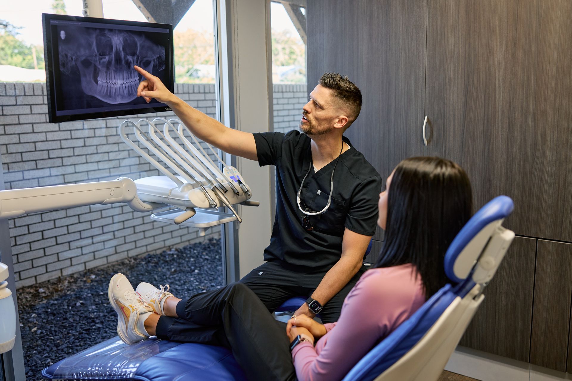 Dentist pointing at an x-ray on a screen, explaining it to a patient in a modern office.