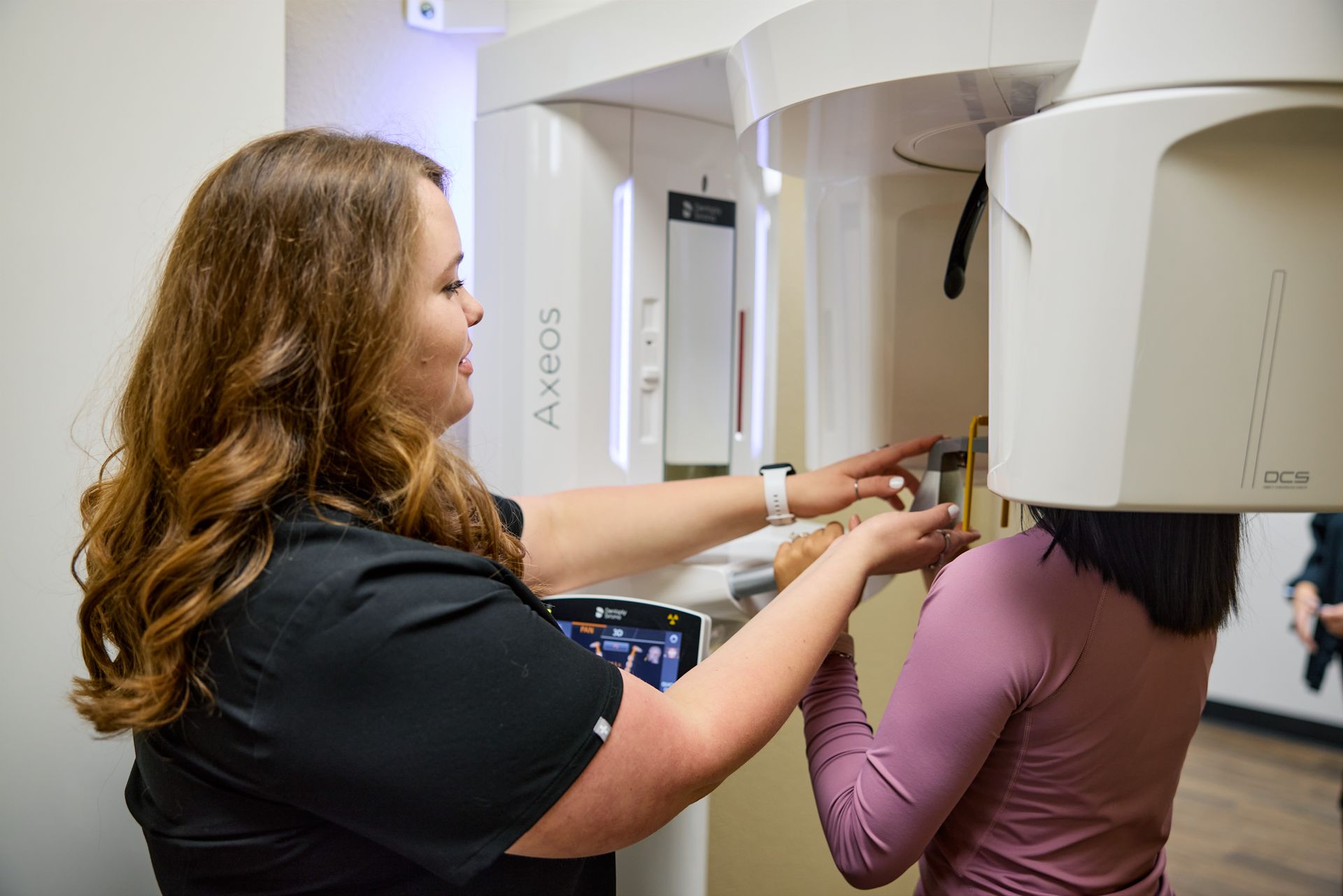 Dental assistant prepares patient for oral scan using a large white imaging machine.