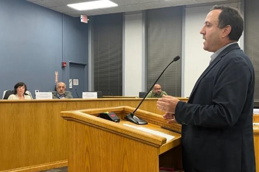 A man standing in front of the microphone with two listener.