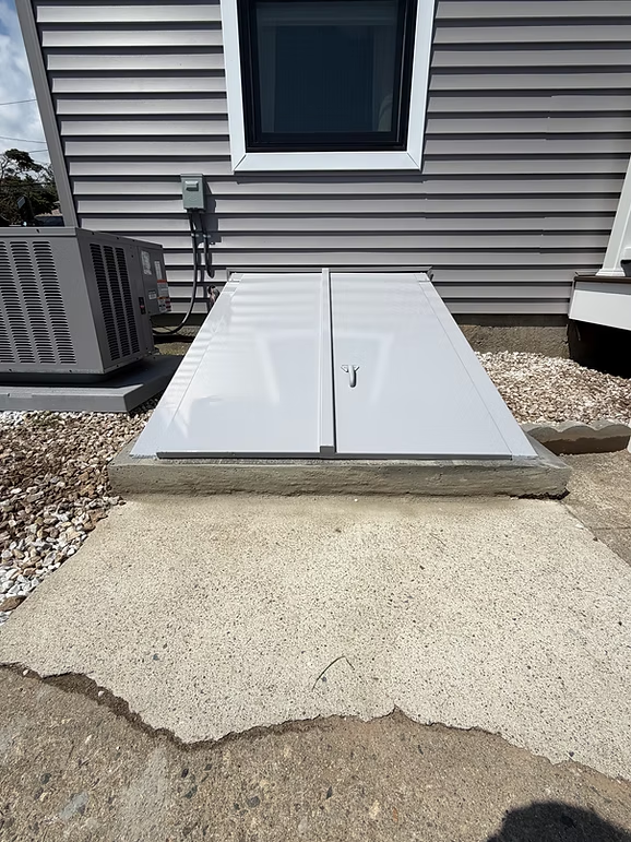 Basement window wells with white covers beside a house exterior and concrete walkway