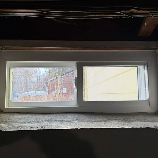 Small basement window with one snowy outdoor view and one bright, blank pane under dark framing