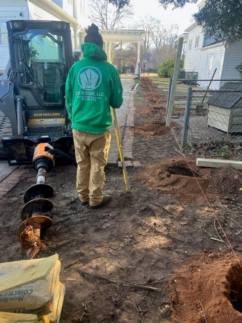 a man in a green hoodie is standing in the dirt next to a tractor .