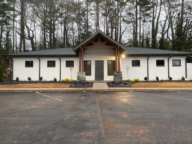 a white house with a black roof is surrounded by trees .