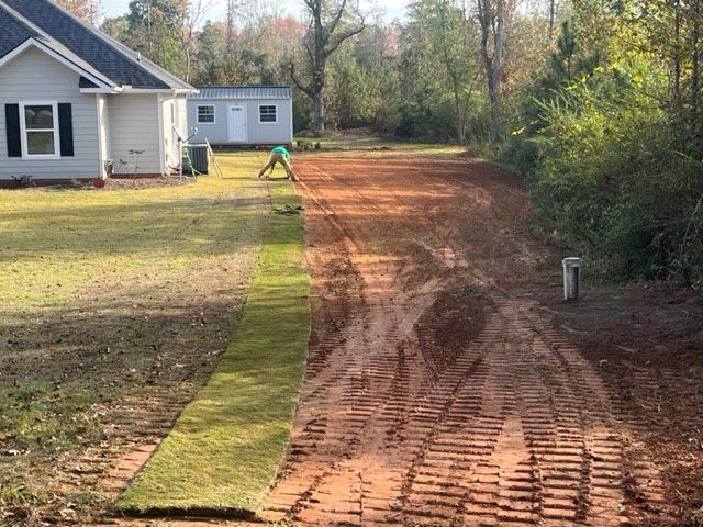 a dirt road leading to a house with a white house in the background .