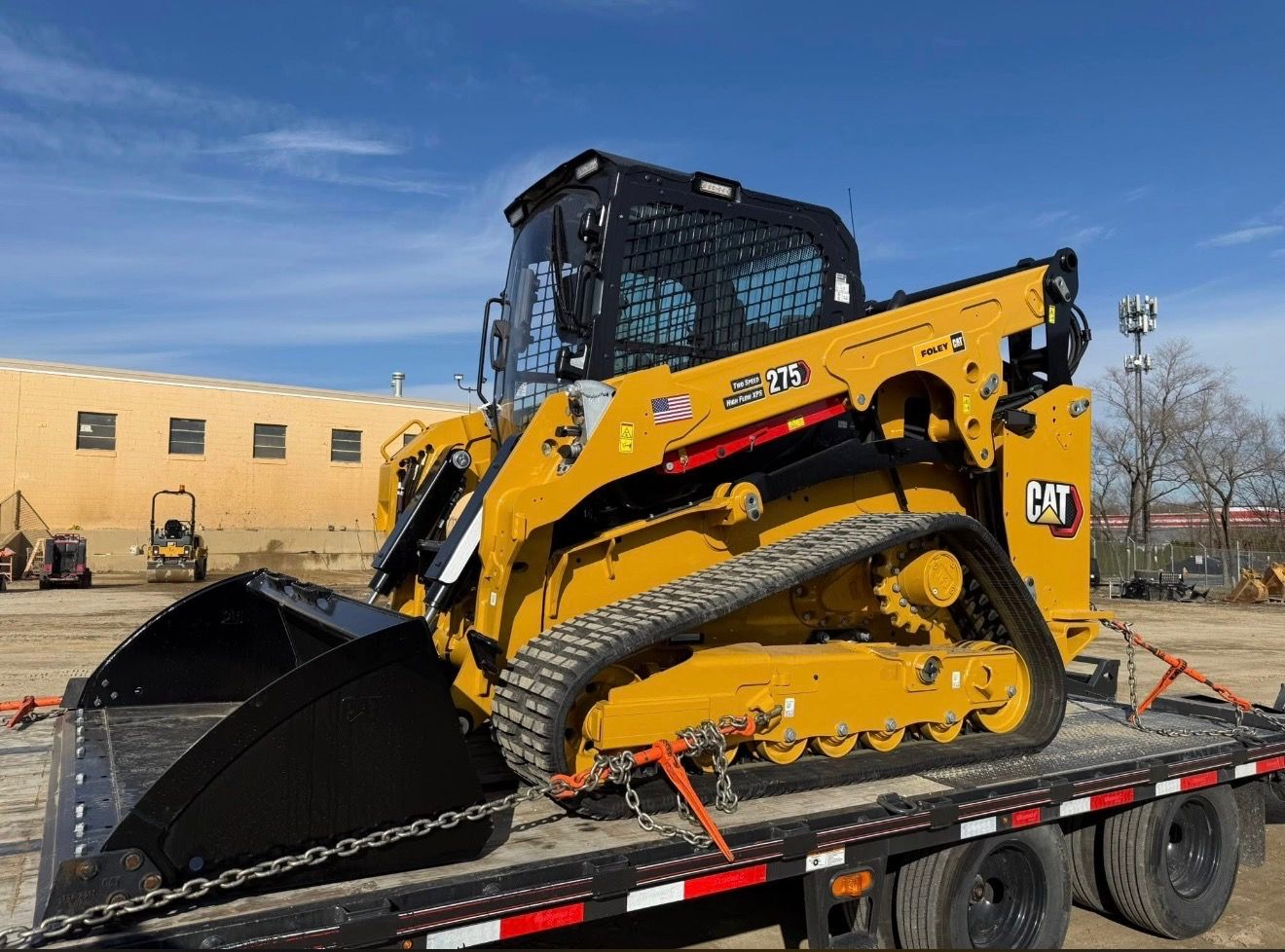 Yellow CAT 299D3 XE compact track loader on a flatbed trailer.