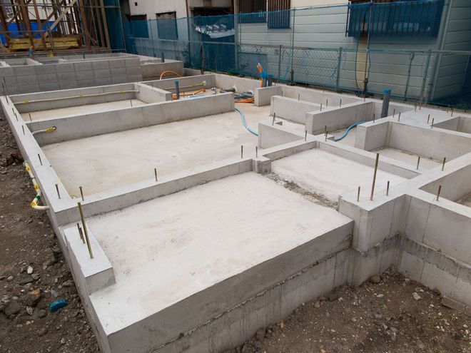 Concrete foundation of a building under construction, with rebar sticking out from the walls.