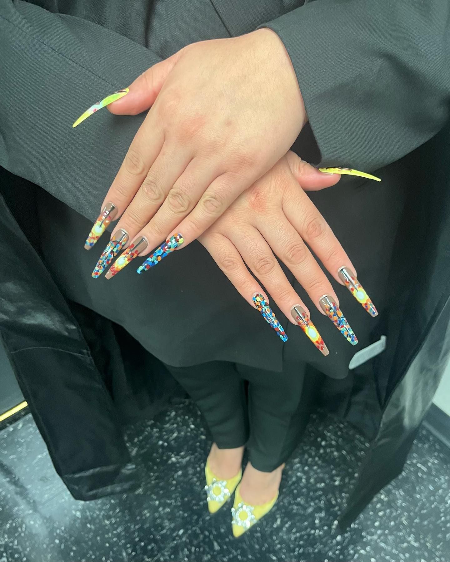 Hands with long, colorful, detailed acrylic nails crossed over body; yellow heels.