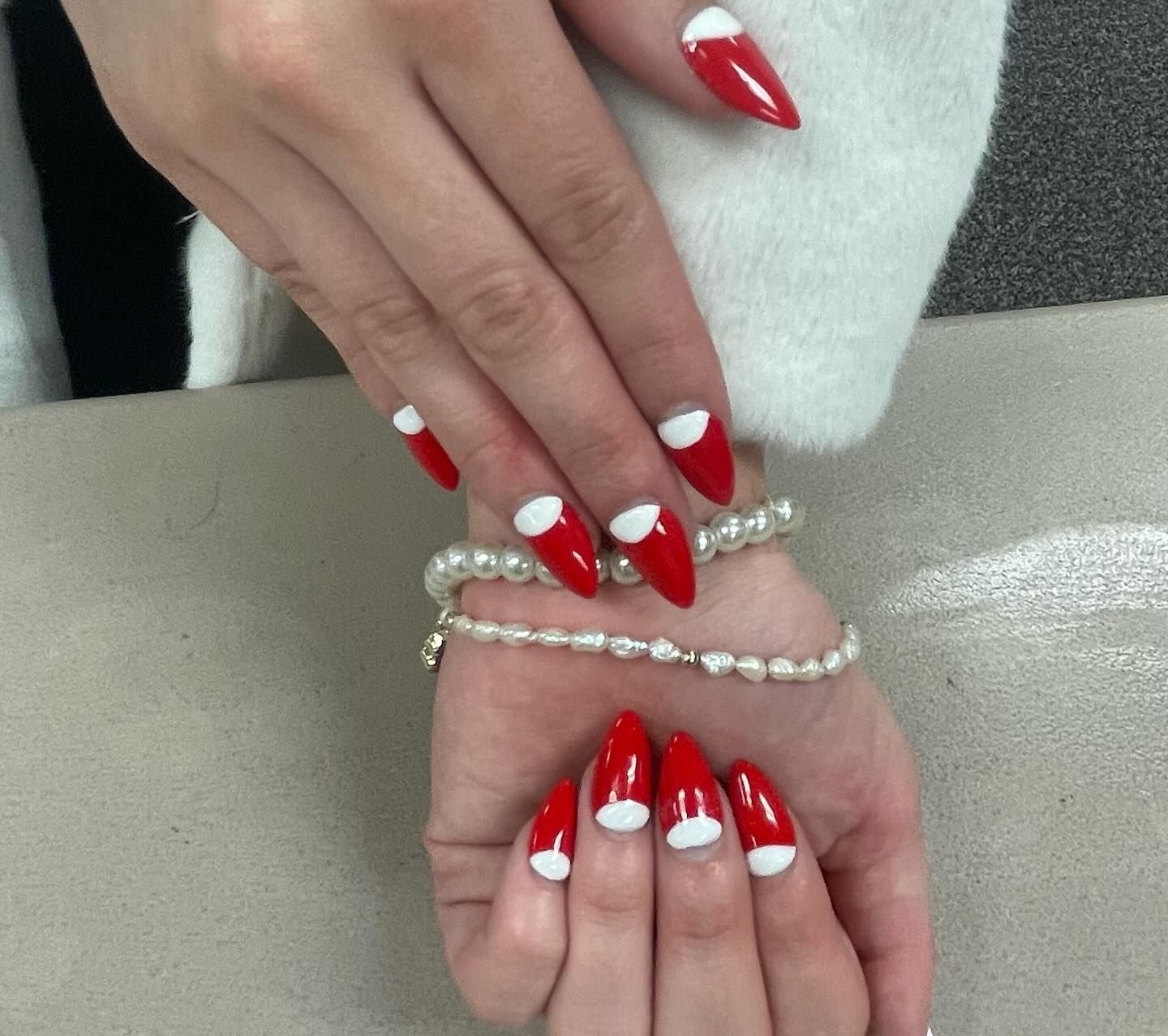 Red and white Santa Claus-themed nail art on a person's hand, wearing a white sweater and a pearl bracelet.