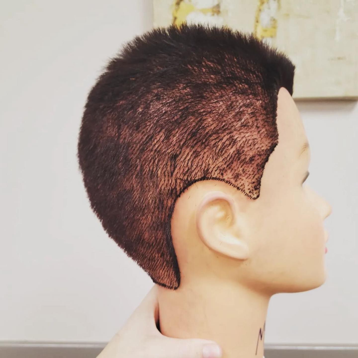 Mannequin head with short dark hair, shaved sides, hand holding head.
