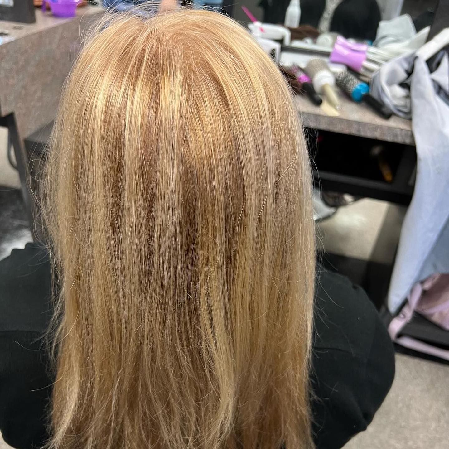 Person with long, blonde hair sitting, likely in a salon. Hair is straight and covers the back and shoulders.