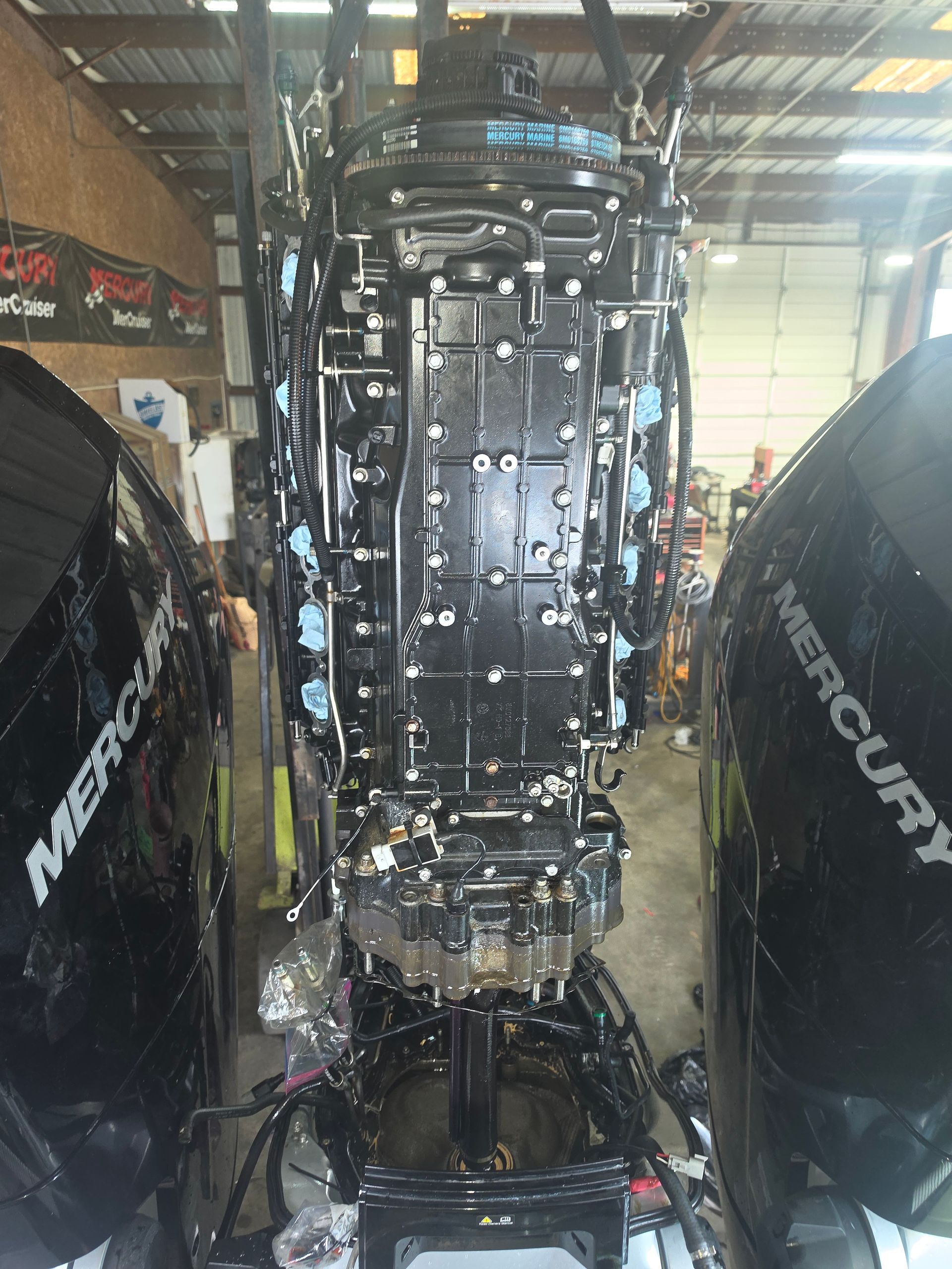 Boat motor in a workshop, viewed from the stern, with black Mercury outboard engines on both sides.