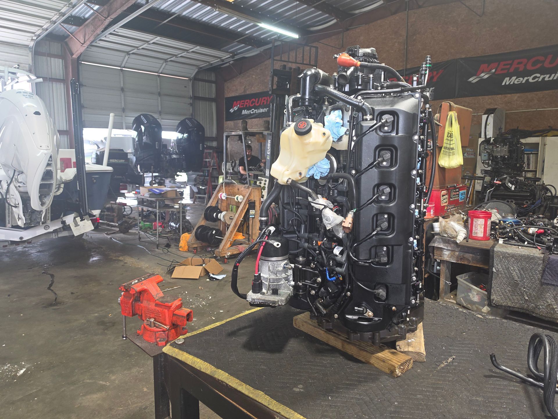 Engine in a cluttered auto shop, with parts and equipment scattered around the workspace.