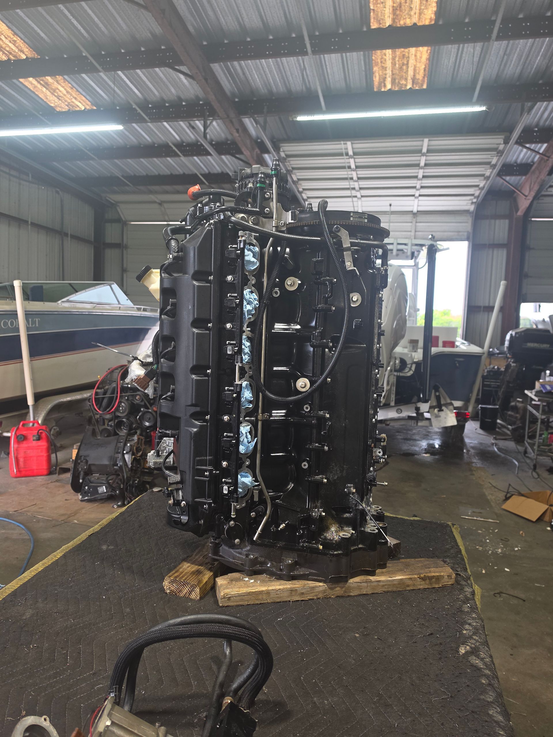 Large black industrial engine standing upright in a workshop garage on a mat, with tools and equipment nearby