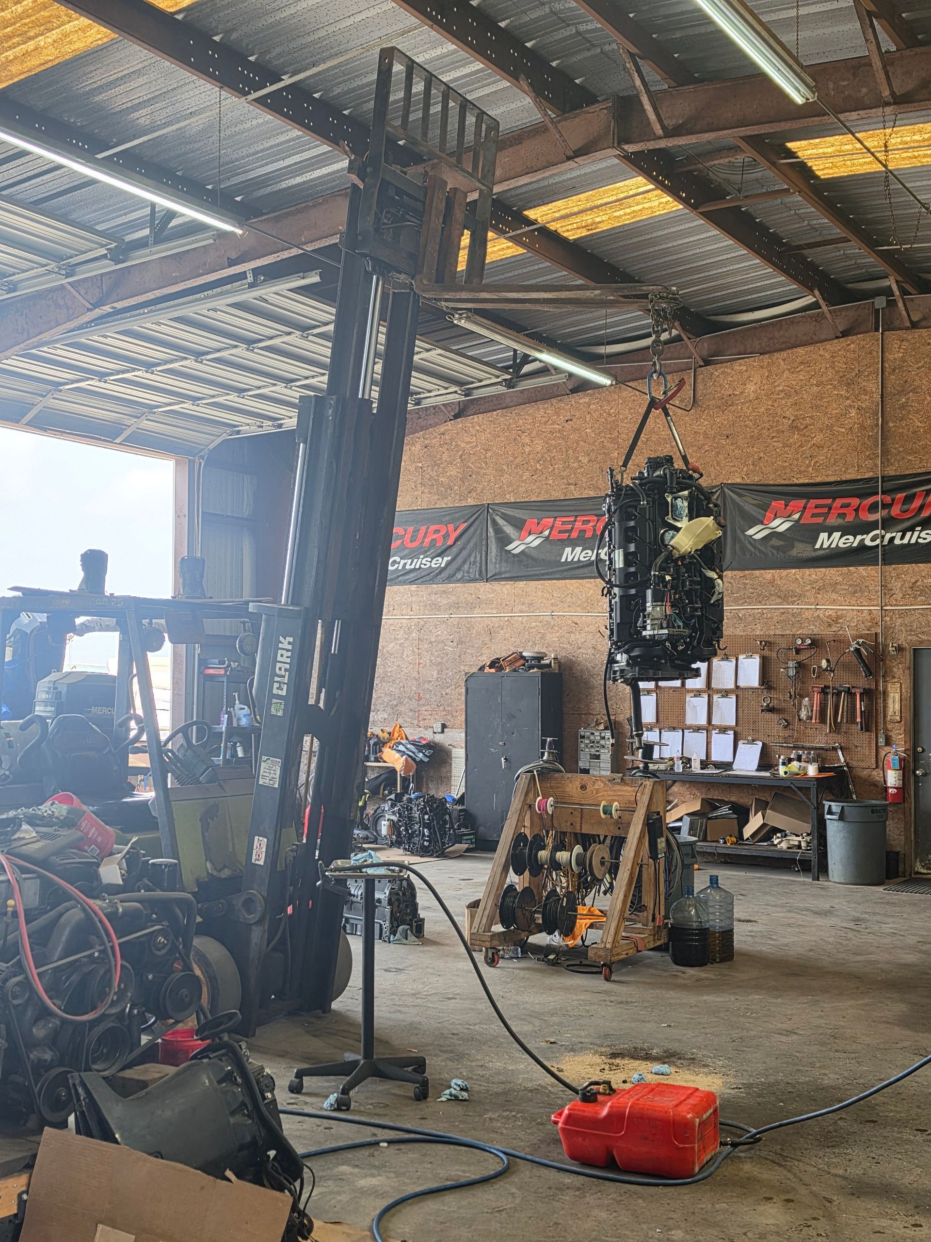 Cluttered workshop with bicycles, tools, hanging decorations, and a red gas can on the floor