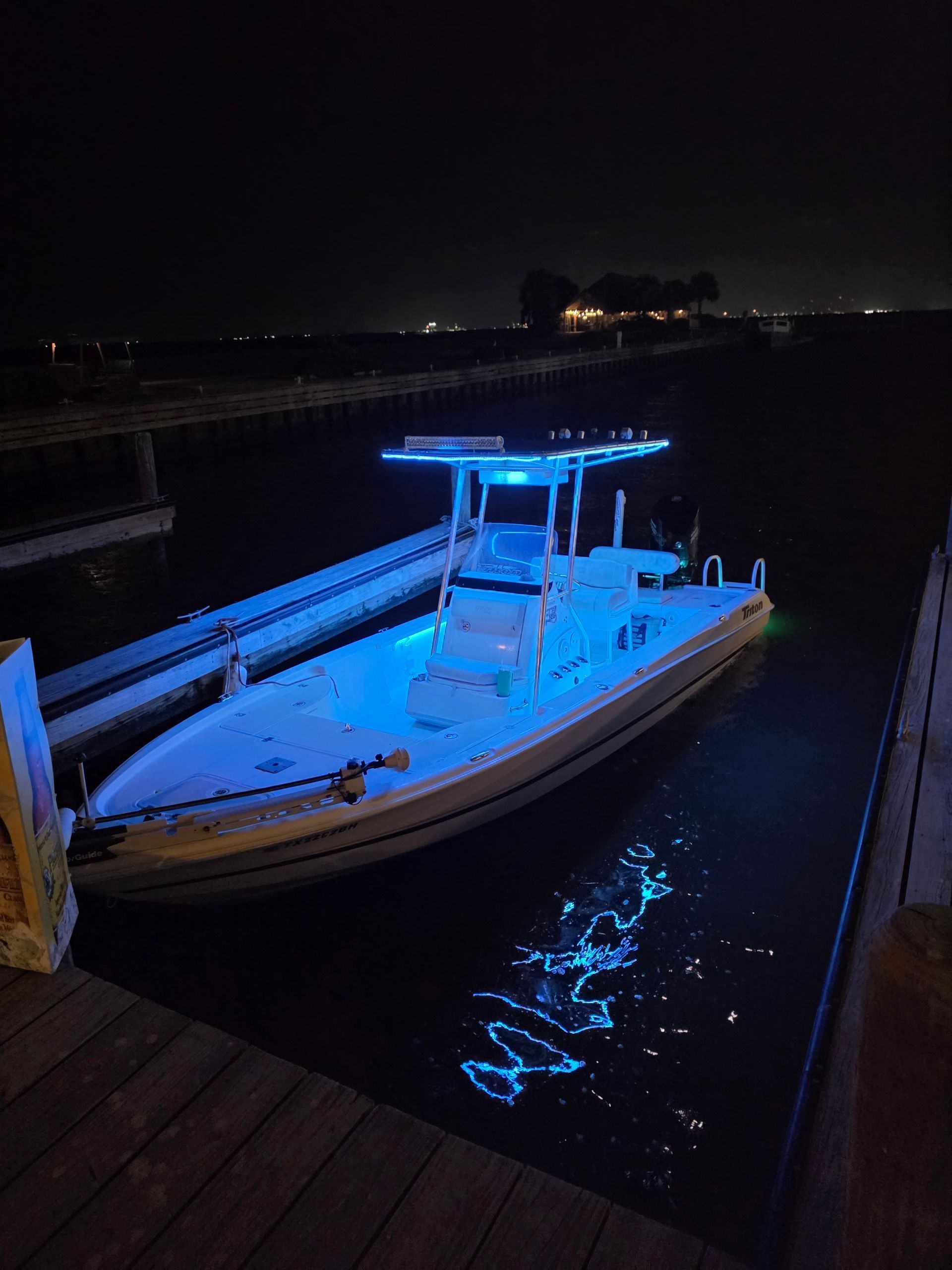 Blue-lit boat docked at night on calm water beside a wooden dock