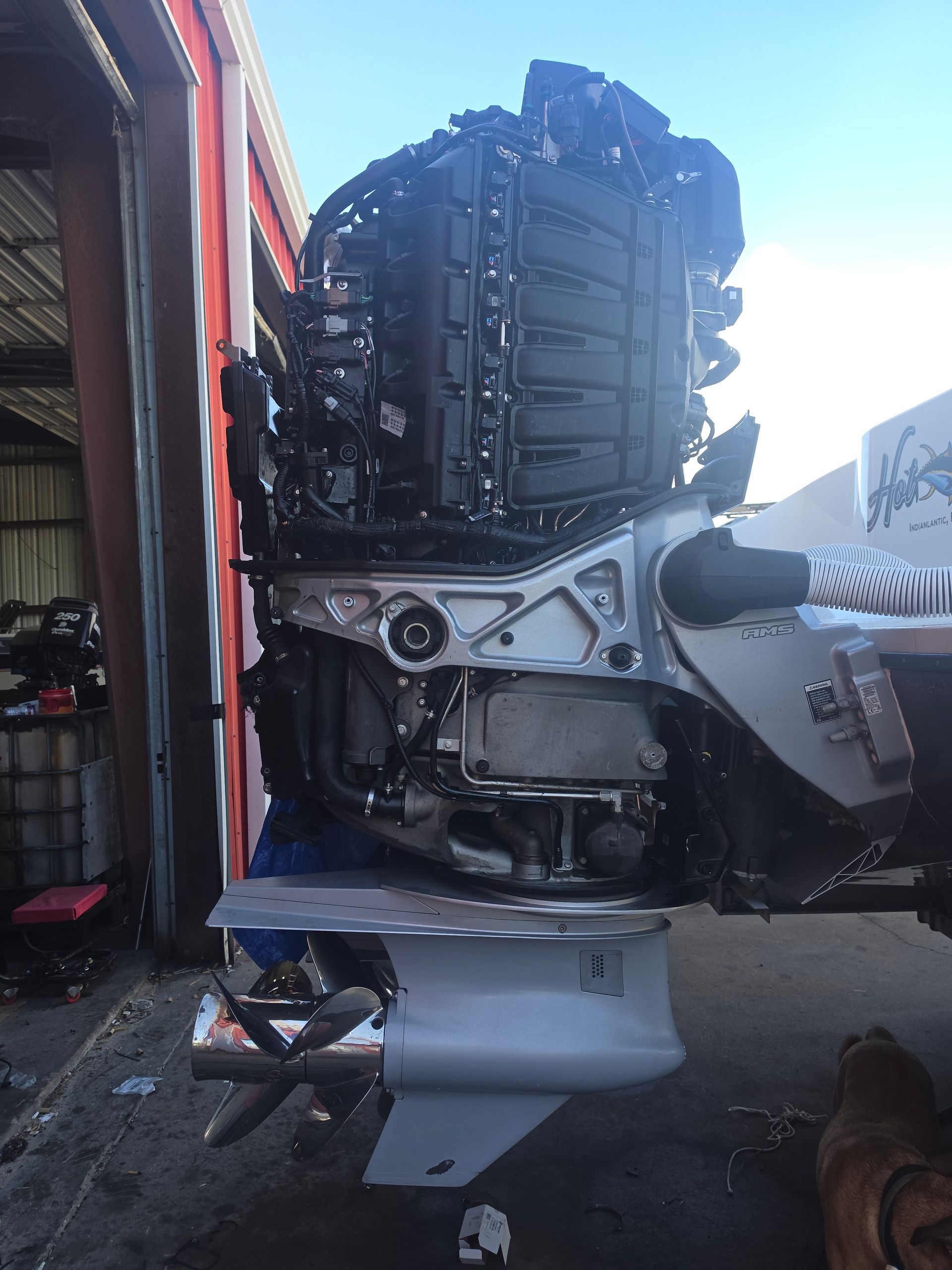 Severely damaged white race car engine and front bodywork beside a building, with a person nearby.