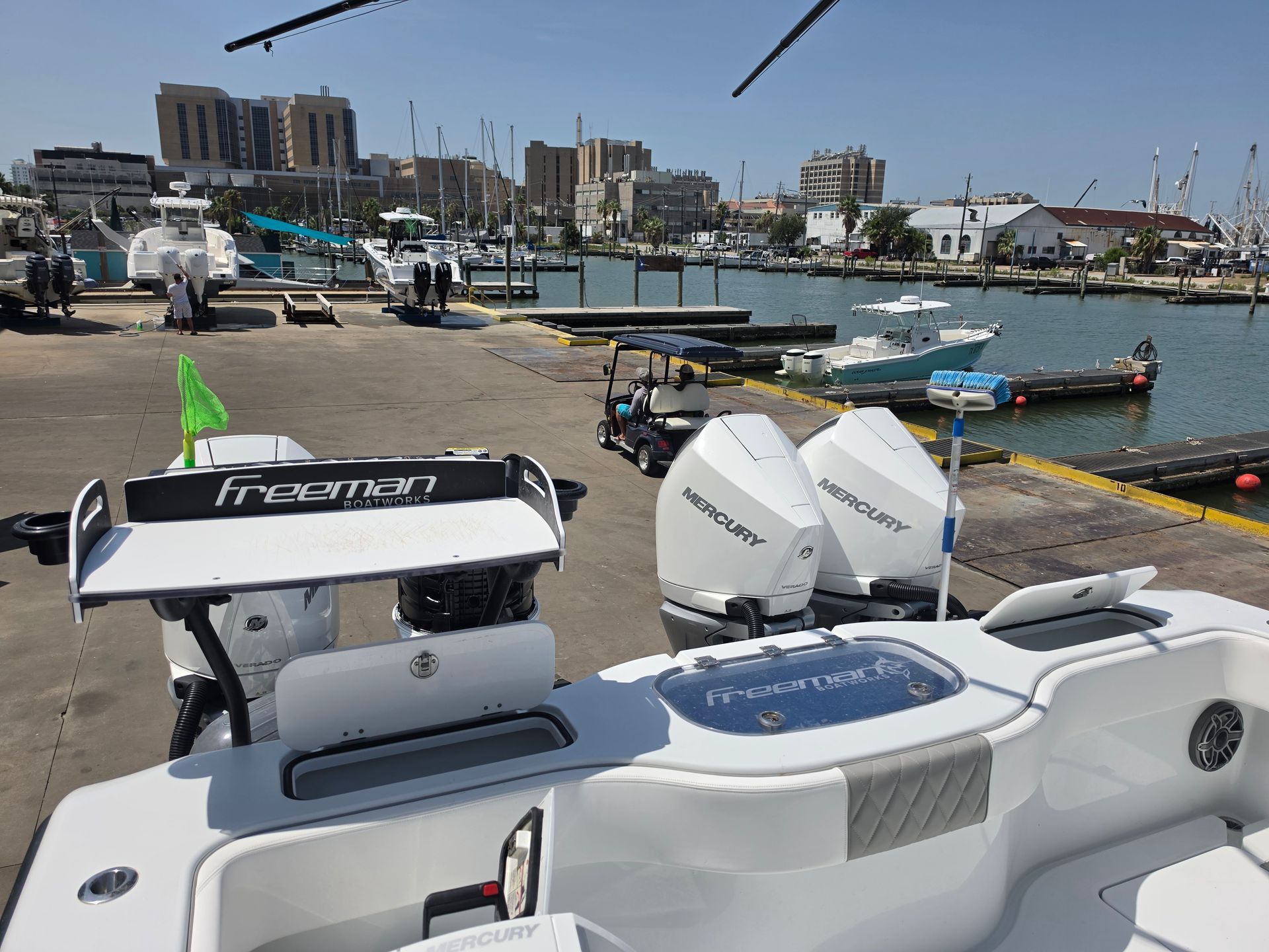 Small motorboats docked at a sunny marina with buildings and cranes in the background.