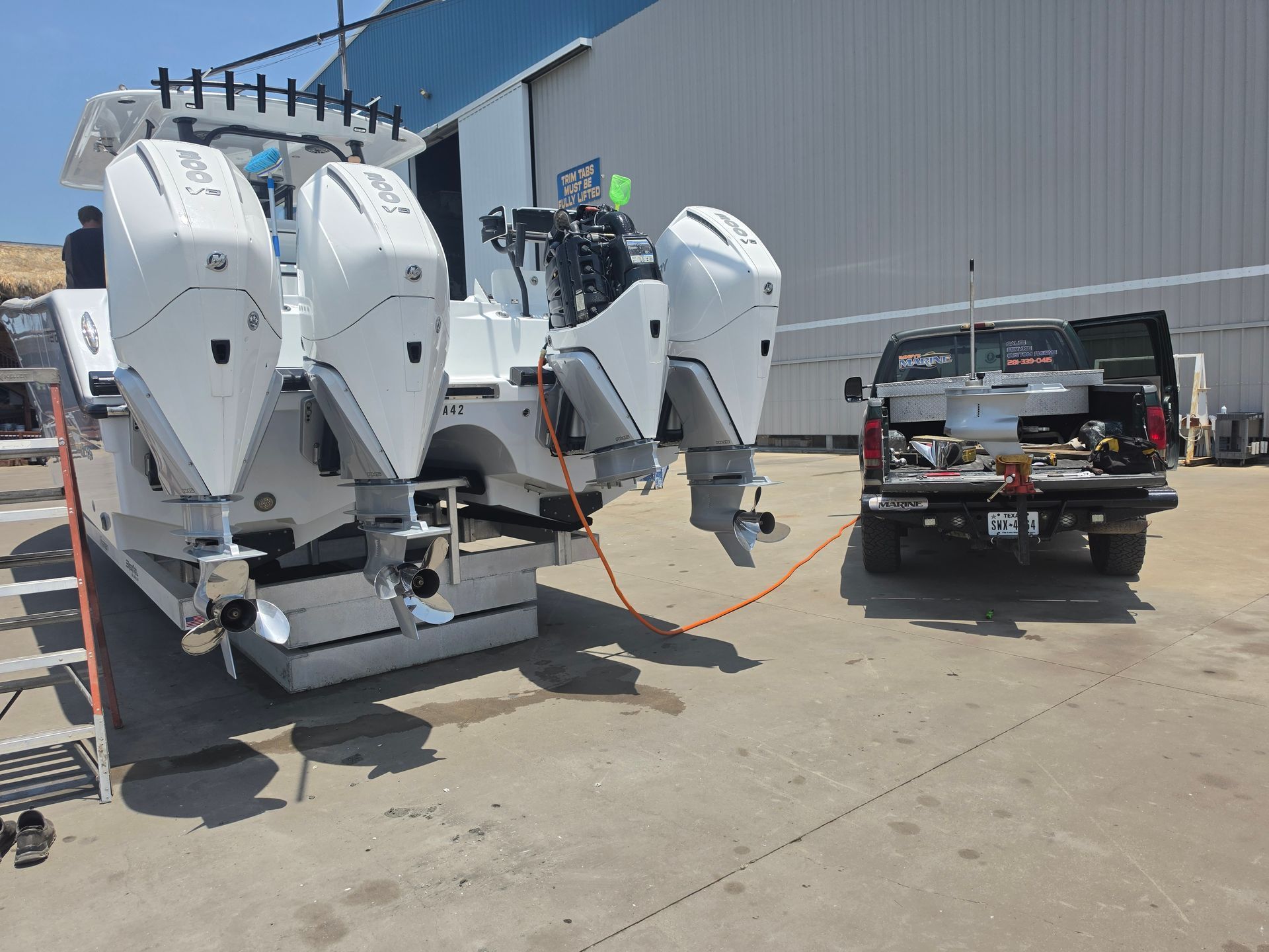 White outboard motors lined up beside a service truck in an industrial lot near a metal building.