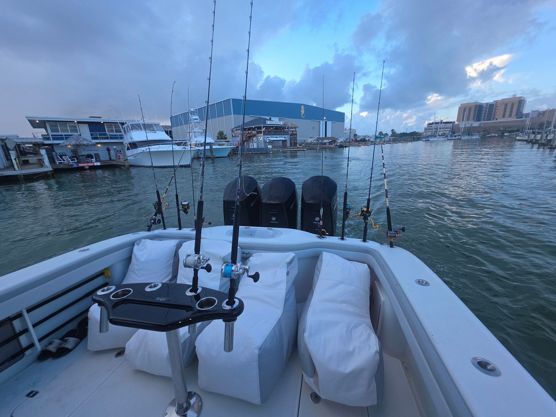 Boat cockpit with white seats and fishing rods, facing a harbor at dusk
