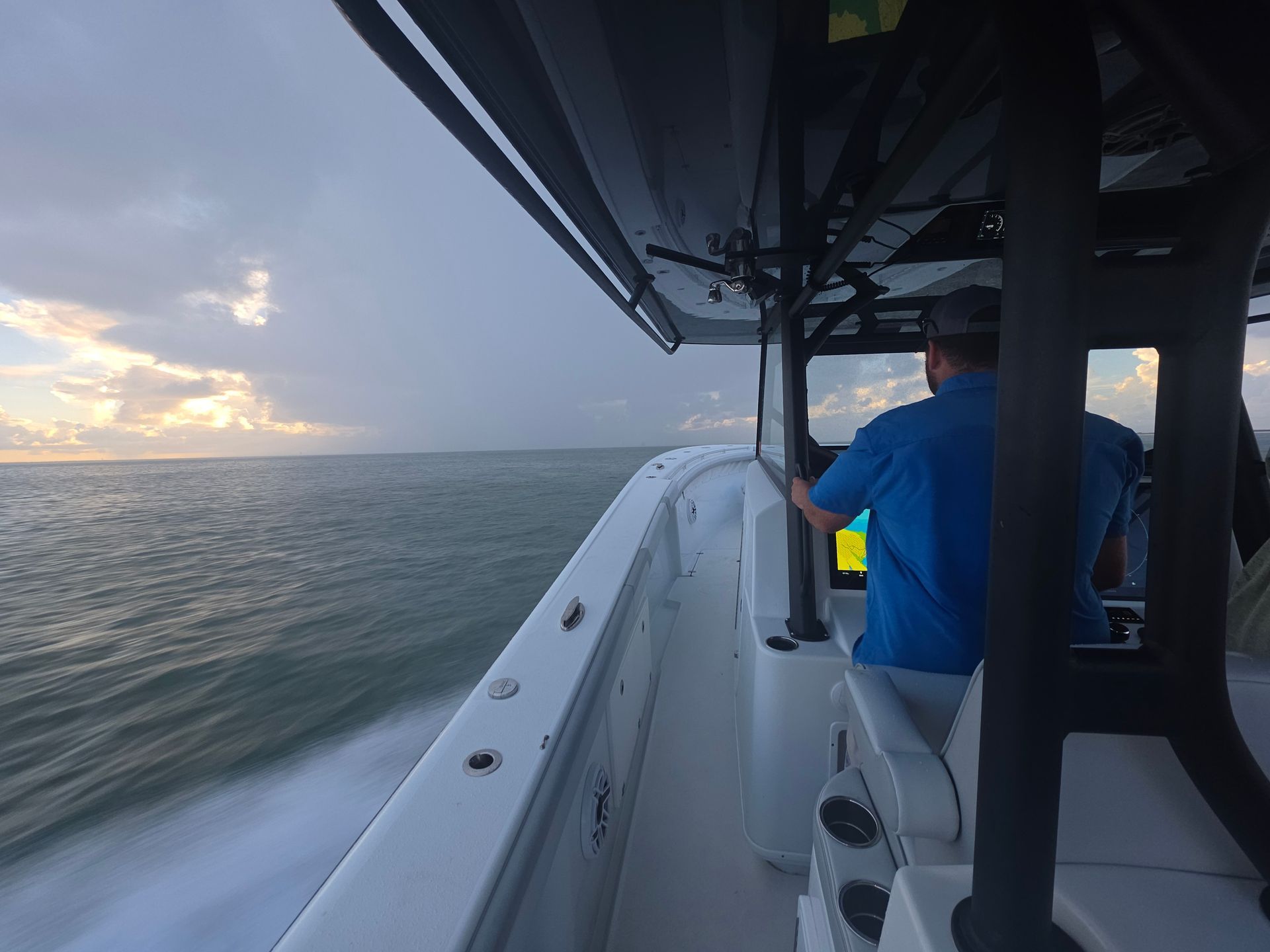 Person in blue jacket on a boat at sunset, looking over choppy water
