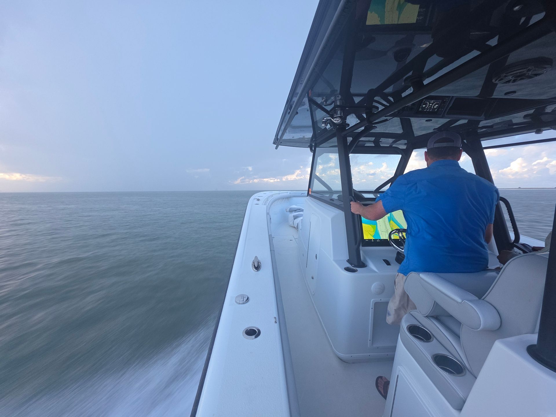 Person steering a white motorboat across calm water at dusk under a cloudy sky