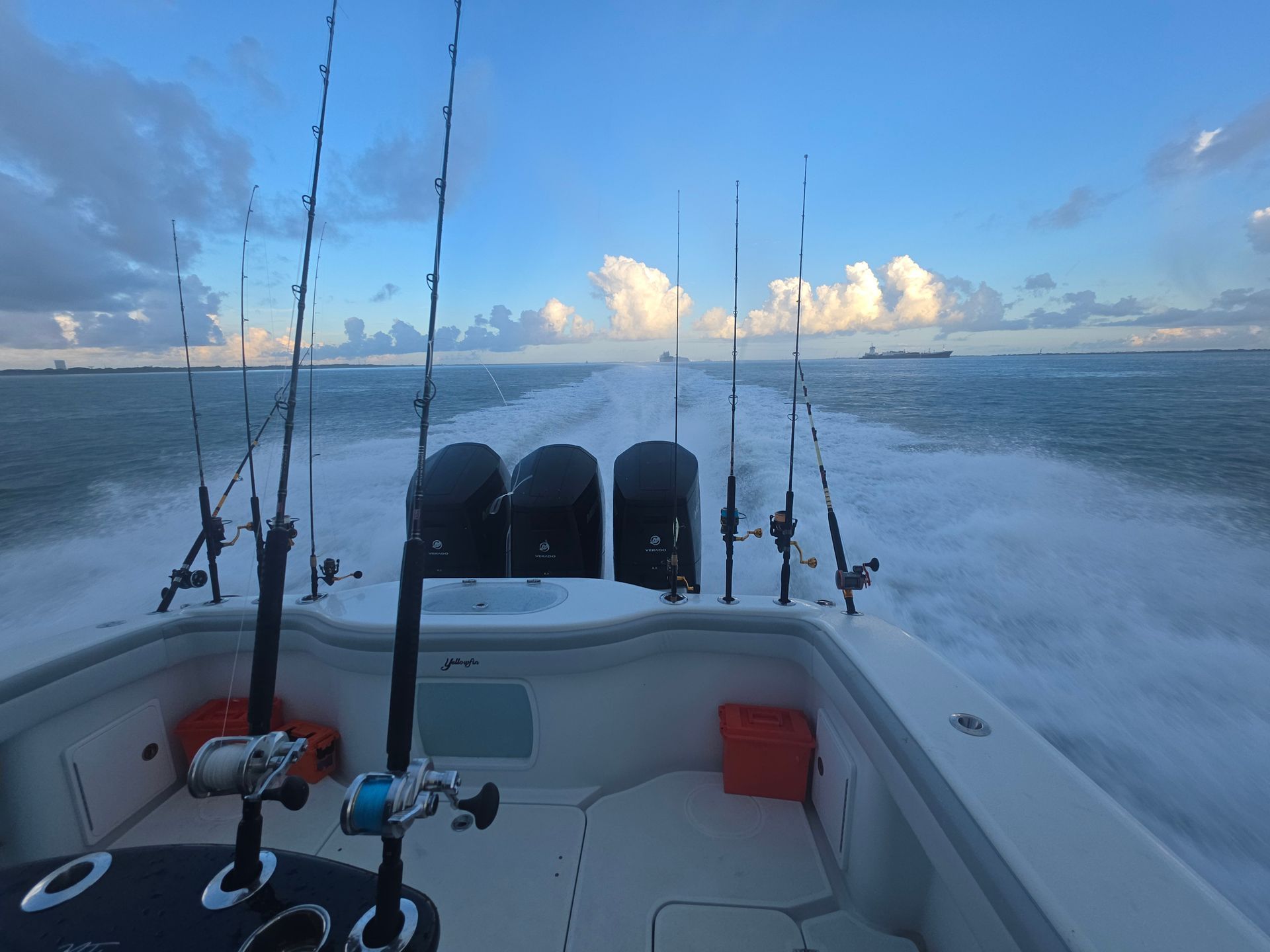 Fishing boat speeding across the ocean at dusk, with rods and twin outboard engines visible from the stern.