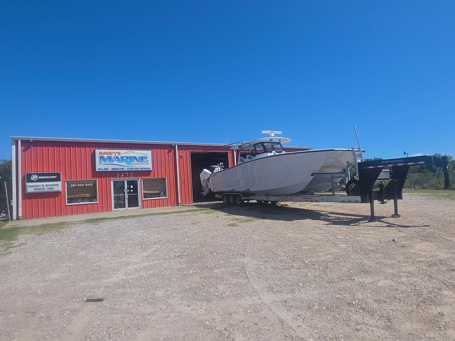 Red building with signs and a large boat on gravel under a clear blue sky