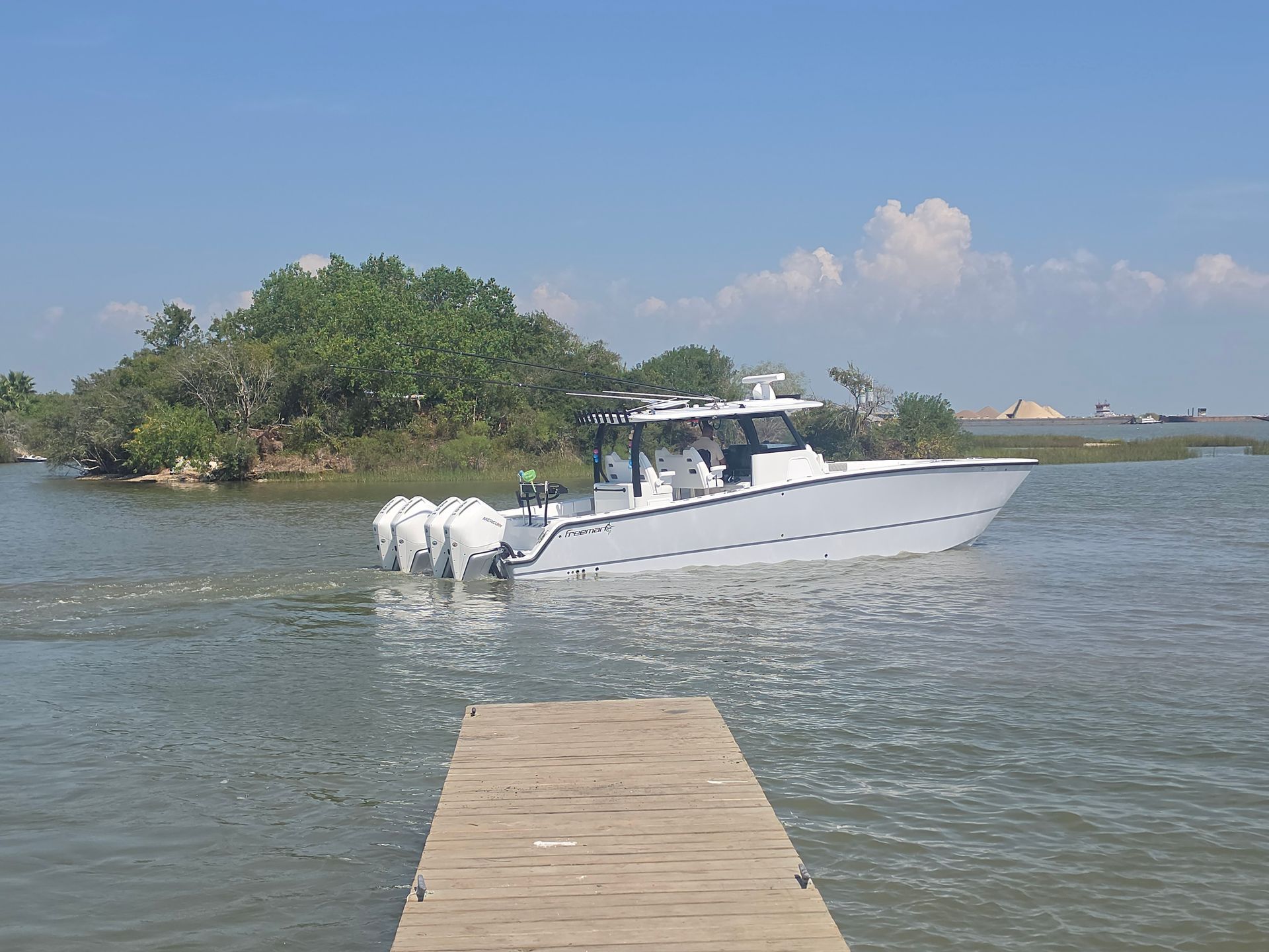 White motorboat near a wooden dock on calm water by a small green island under a blue sky