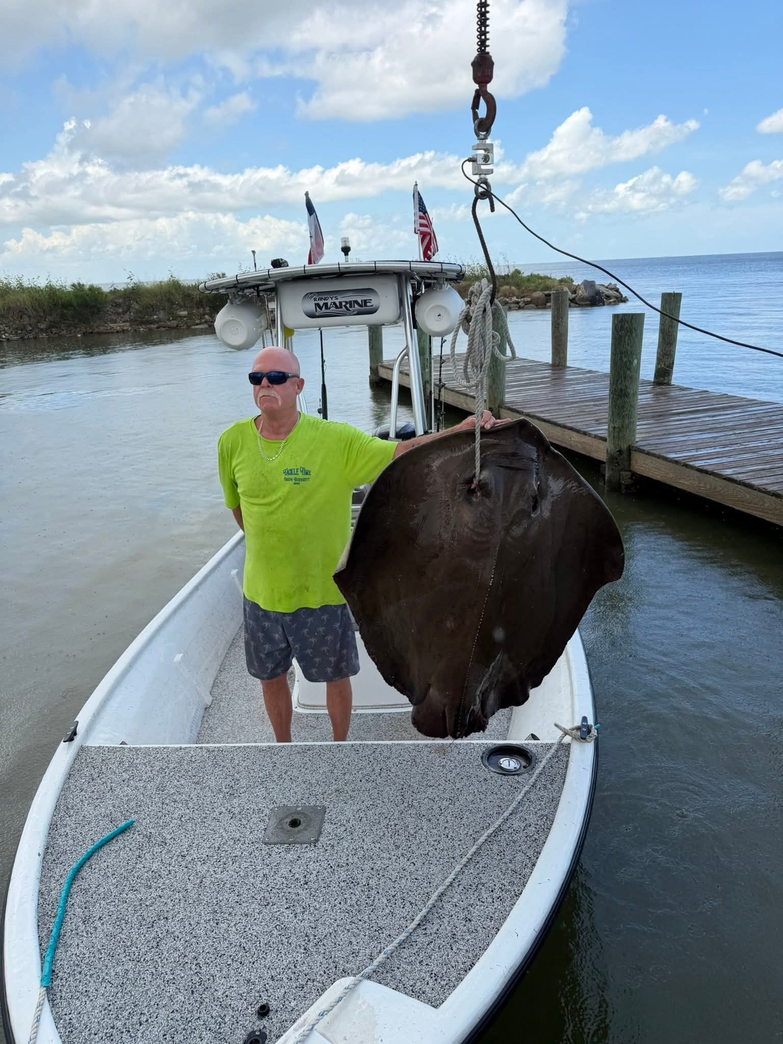 Man standing on a boat beside a large fish hanging from a crane over the water