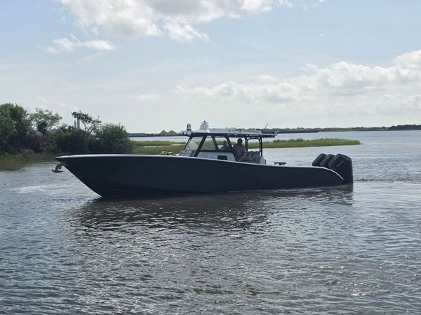 Black motorboat on calm water near a grassy shoreline under a partly cloudy sky