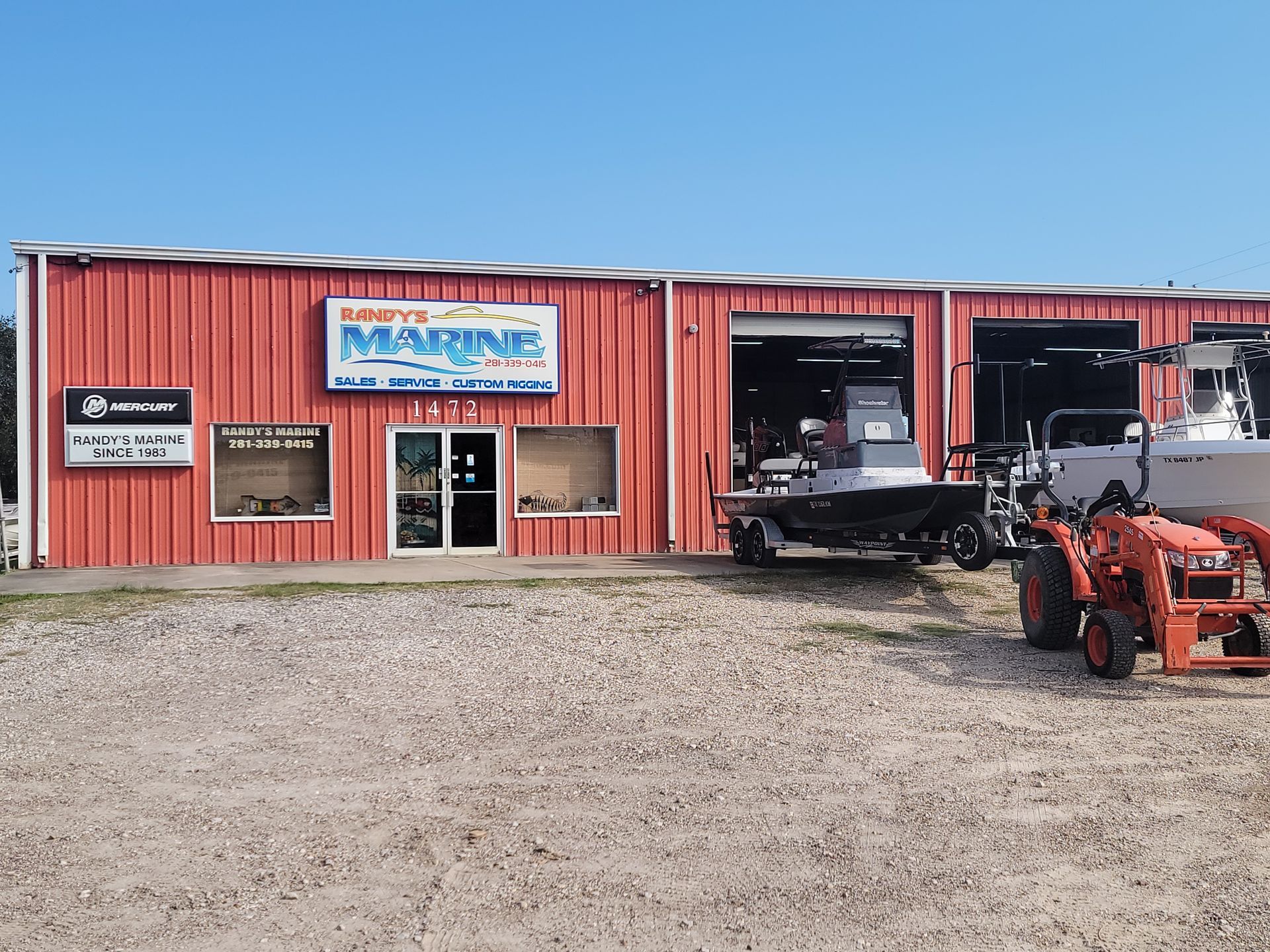 Red marine shop with boats, a tractor, and a clear blue sky.